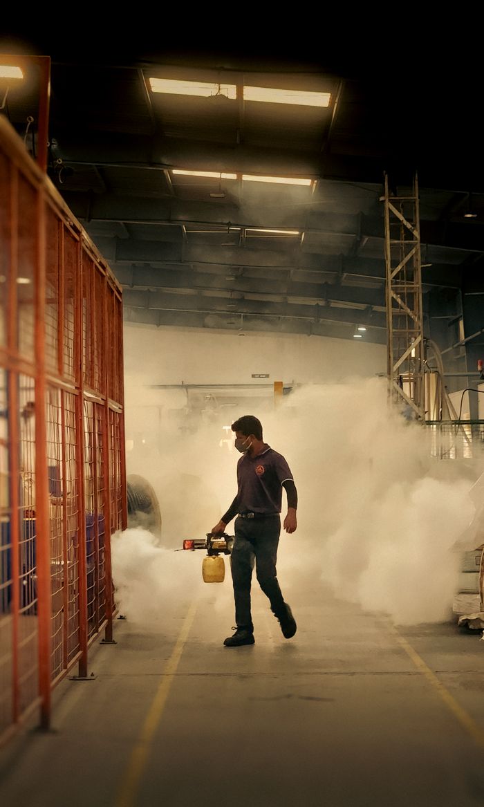 Worker fumigating inside a warehouse using a fogging machine for pest control.